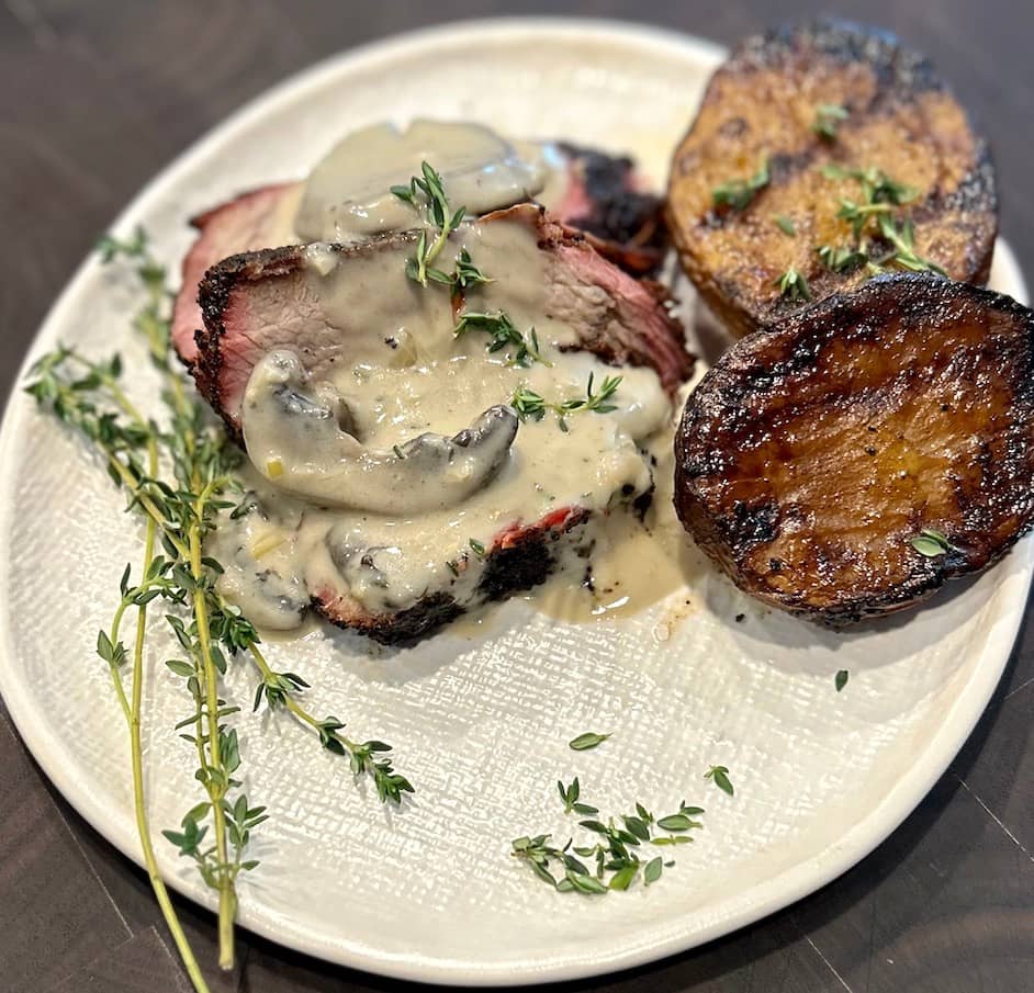 Coffee Rubbed Tri-Tip Steak with Mushroom Bourbon Cream sauce plated and garnished with fresh thyme.
